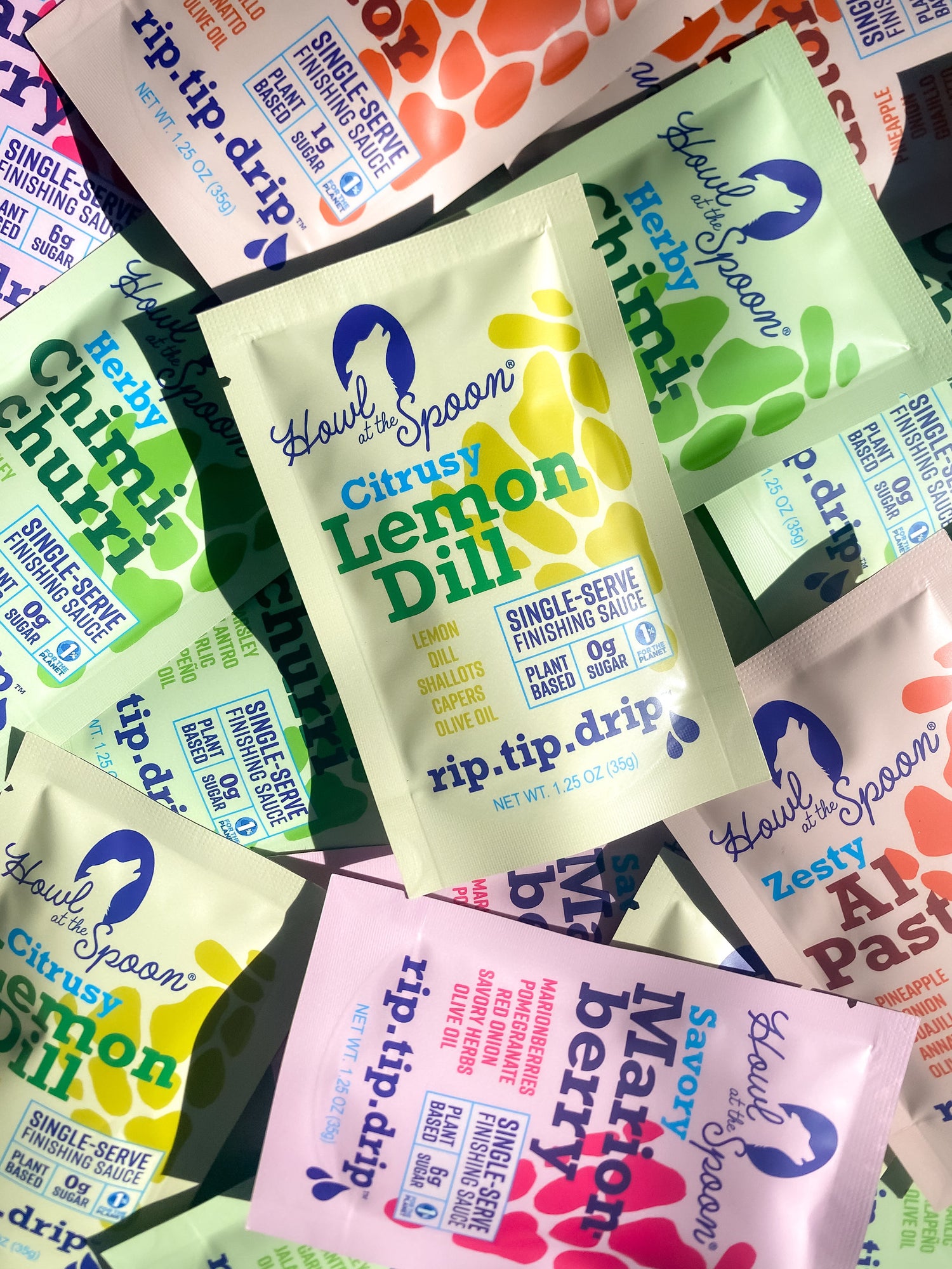 Assorted single-serve sauce packets from Howl at the Spoon—Al Pastor, Chimichurri, Lemon Dill, and Marionberry—scattered on a textured surface.”