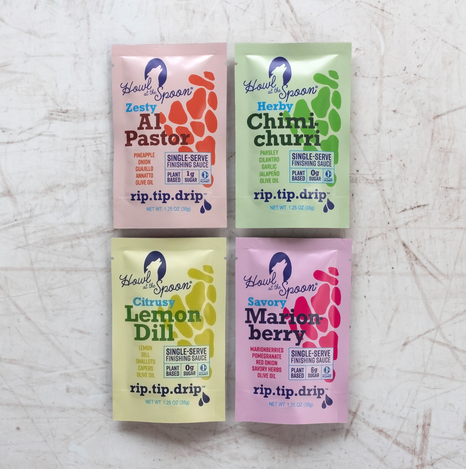 Flat lay of four colorful single-serve sauce packets from Howl at the Spoon—Al Pastor, Chimichurri, Lemon Dill, and Marionberry—arranged on a modern background